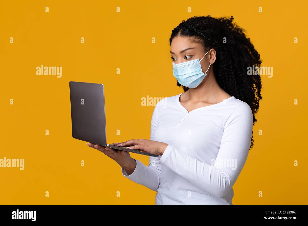 Lavoro remoto durante la pandemia. Giovane donna nera in maschera medica Holding portatile Foto Stock
