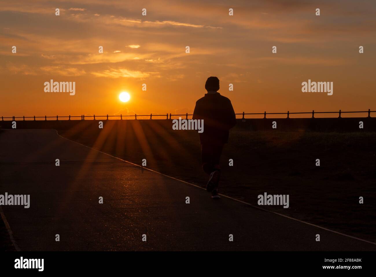 Jogger maschio che corre verso il sole all'alba. Corsa di mattina presto. Dawn Run. Lone Runner, jogging verso il sole che sorge nel Gunners Park, Shoeburyness Foto Stock