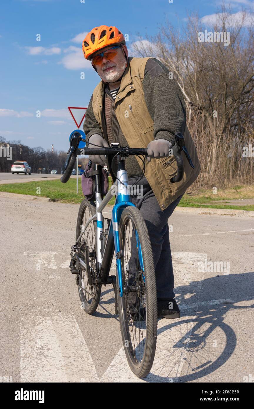 Ritratto all'aperto di un uomo anziano barbuto e chubby pronto a cavalcare in bicicletta ghiaiosa Foto Stock