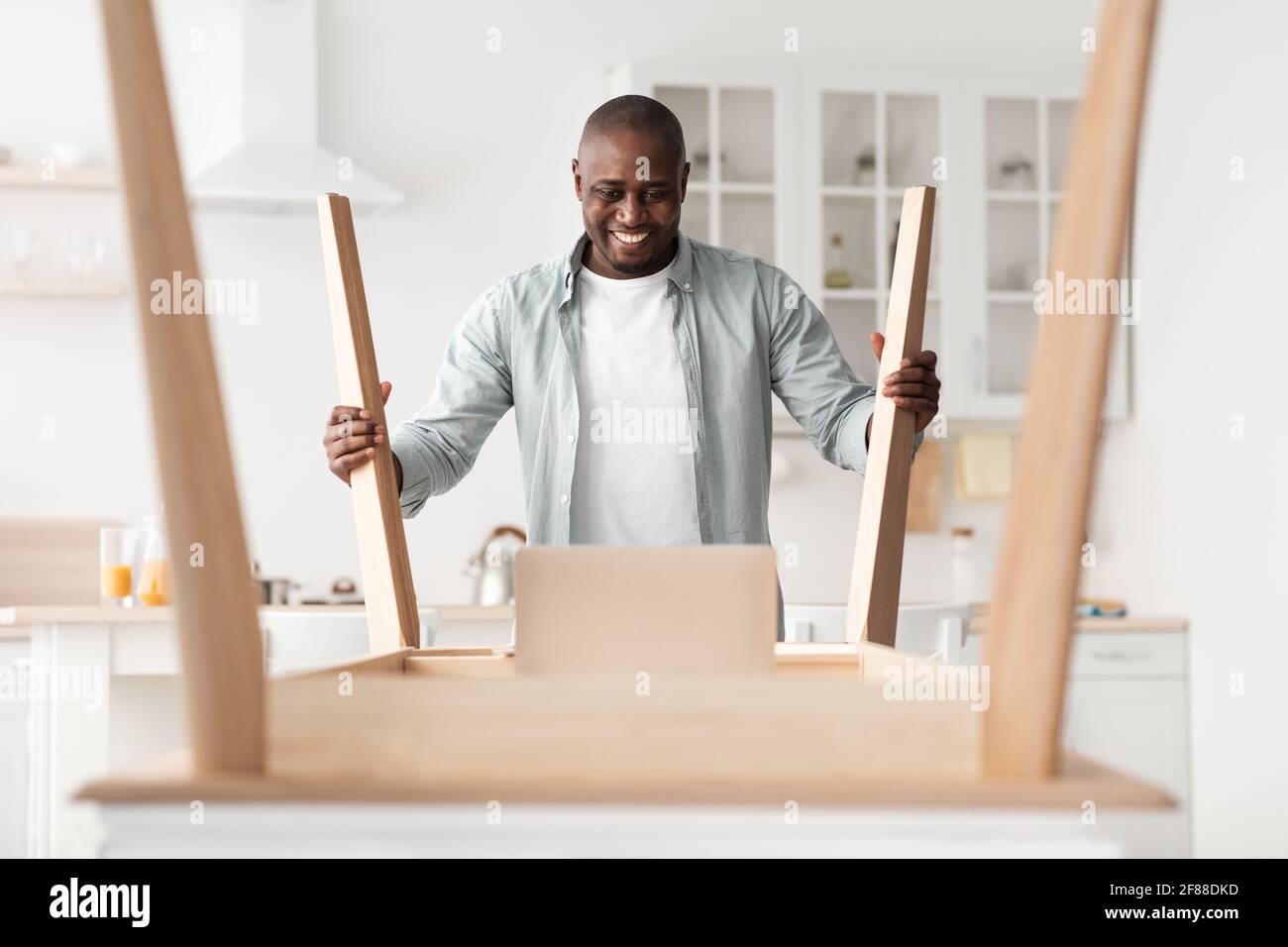 Eccitato afroamericano uomo essere felice di installare scrivania di legno da soli dopo il trasferimento a casa Foto Stock
