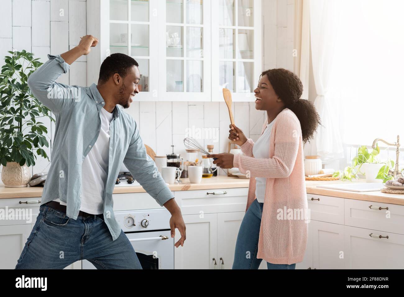 Divertimento domestico. I coniugi neri combattono giocosamente in cucina, usando le spatole come armi Foto Stock