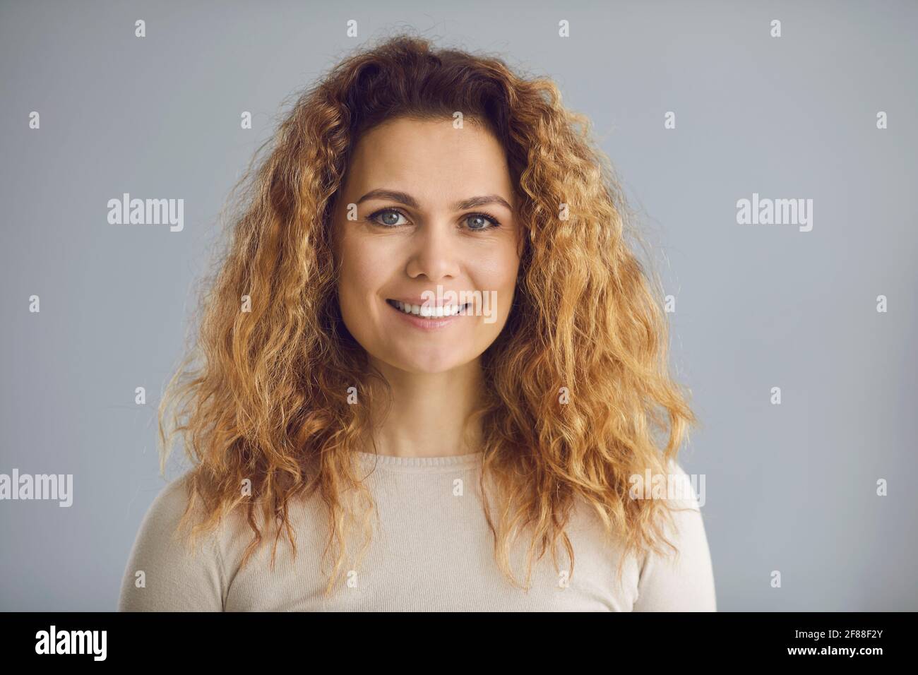 Studio Head shot di una donna felice con lungo ondulato capelli e un sorriso bianco amichevole Foto Stock