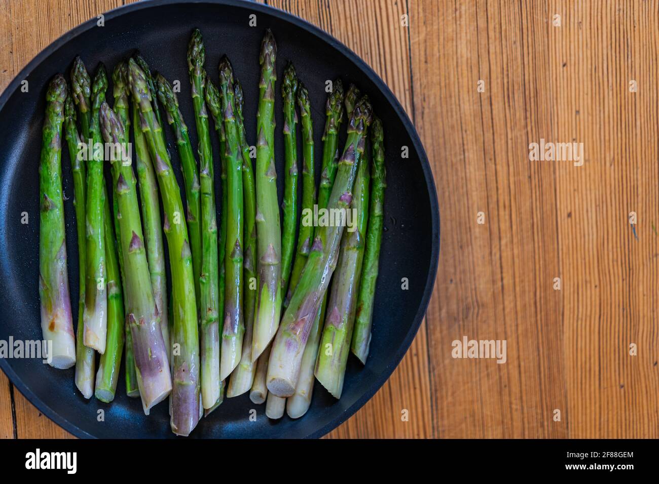 Asparagi verdi fritti in padella nera su fondo di legno. Vista dall'alto, spazio di copia. Foto Stock