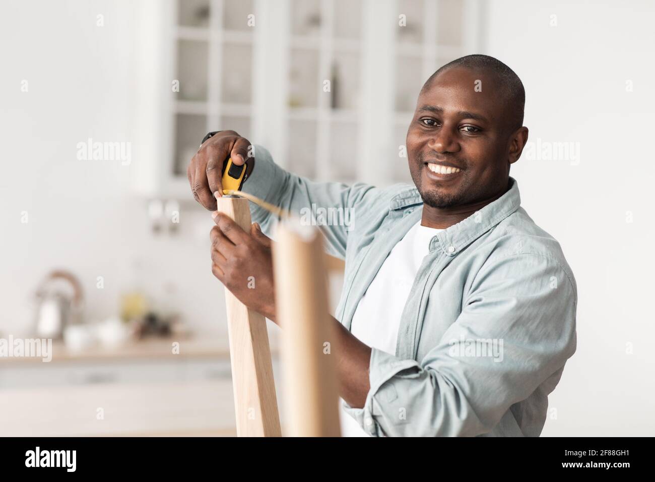Handyman afroamericano che misura la larghezza tra le gambe del tavolo di legno, assemblando nuovi mobili a casa Foto Stock