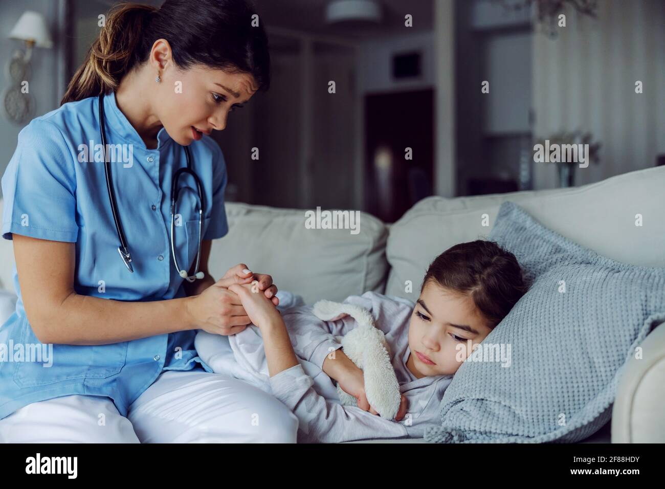Bambina malata che si trova a letto a casa mentre l'infermiera tiene la mano. Infermiera che conforta la bambina malata. Foto Stock