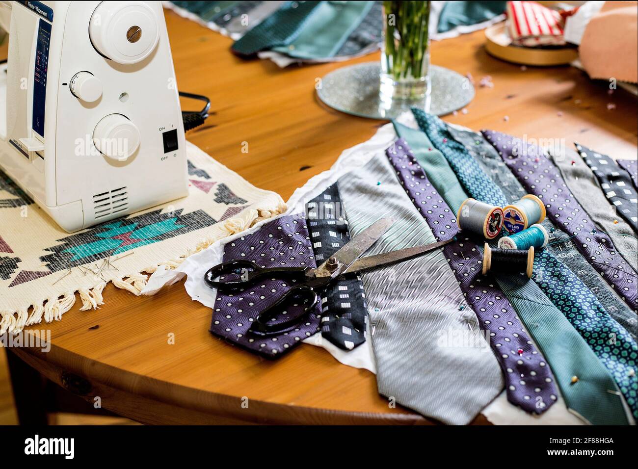 Un tavolo da pranzo con macchina da cucire e materiali compresi forbici e bobine di filo di cotone. Foto Stock