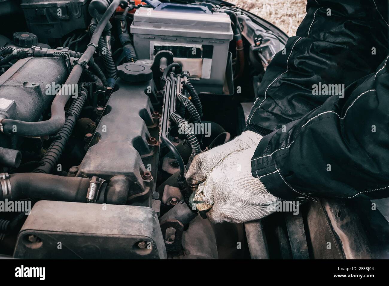 Sostituzione dei fili ad alta tensione su un motore di automobile. L'uomo meccanico che ripara un veicolo vecchio è in servizio. Aprire il cofano automatico Foto Stock