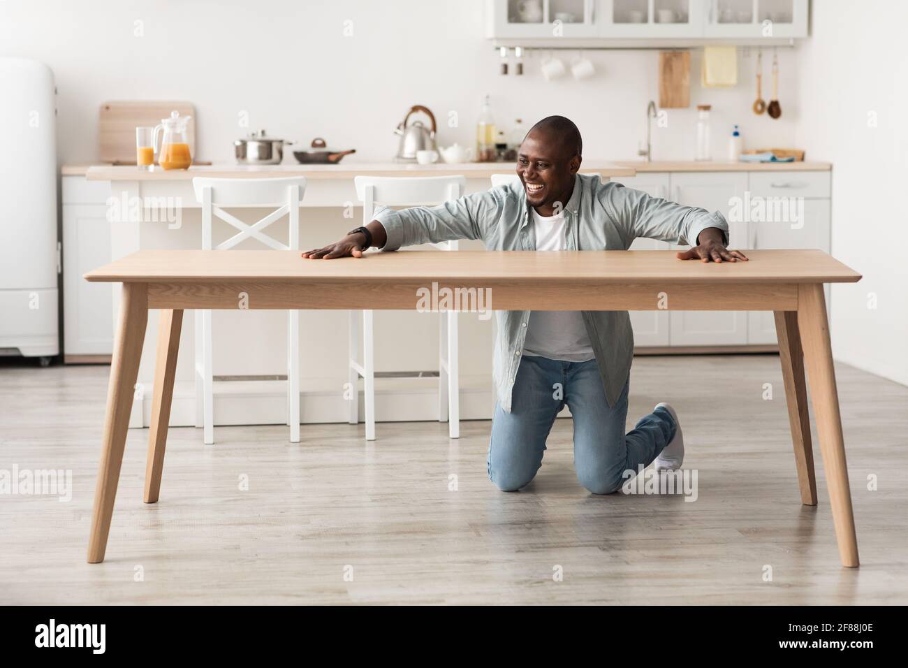 Uomo nero sopravorato che tocca il nuovo tavolo di legno, dopo aver assembiato mobili con le proprie mani a casa in cucina interno Foto Stock