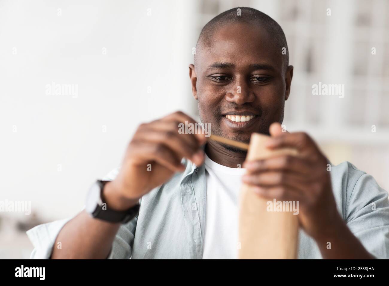 Eccitato afroamericano uomo assemblare nuovo tavolo di legno con bullone, facendo da soli dopo la ristrutturazione Foto Stock