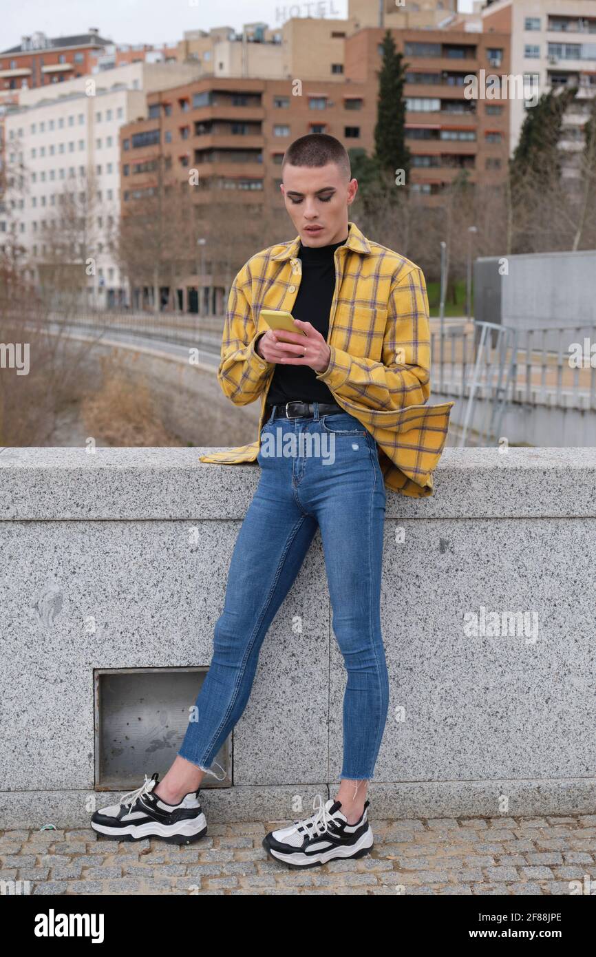 Giovane non binaria che chiacchiera su uno smartphone infastidito. Make up persona androgina. Foto Stock