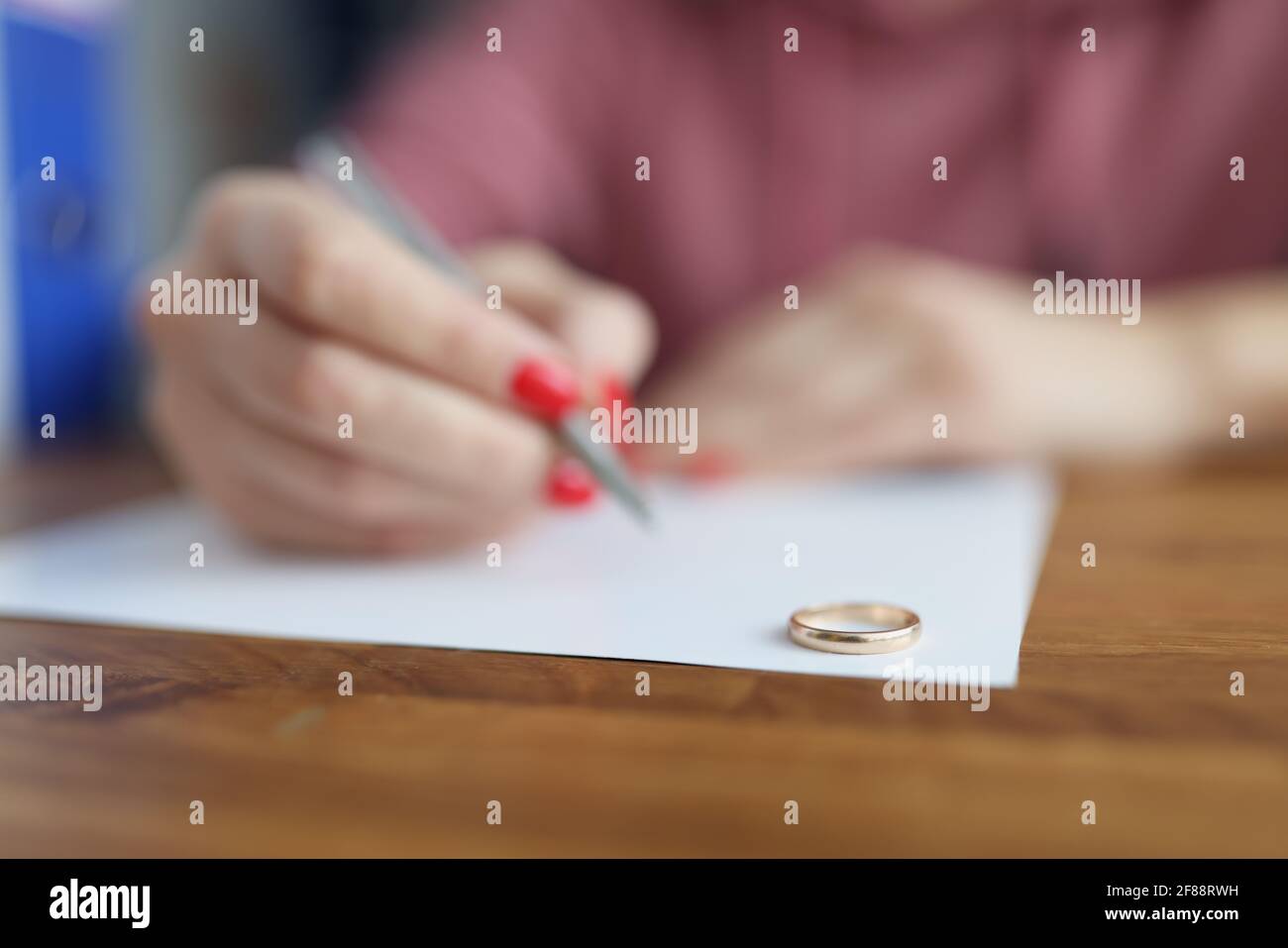 La mano della donna che scrive la dichiarazione di divorzio sullo sfondo del matrimonio primo piano degli anelli Foto Stock