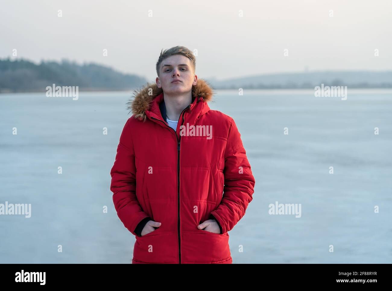 Un ragazzo adolescente, in una giacca rossa, pone e riflette emotivamente sulla vita, sullo sfondo di un lago ghiacciato. Foto Stock