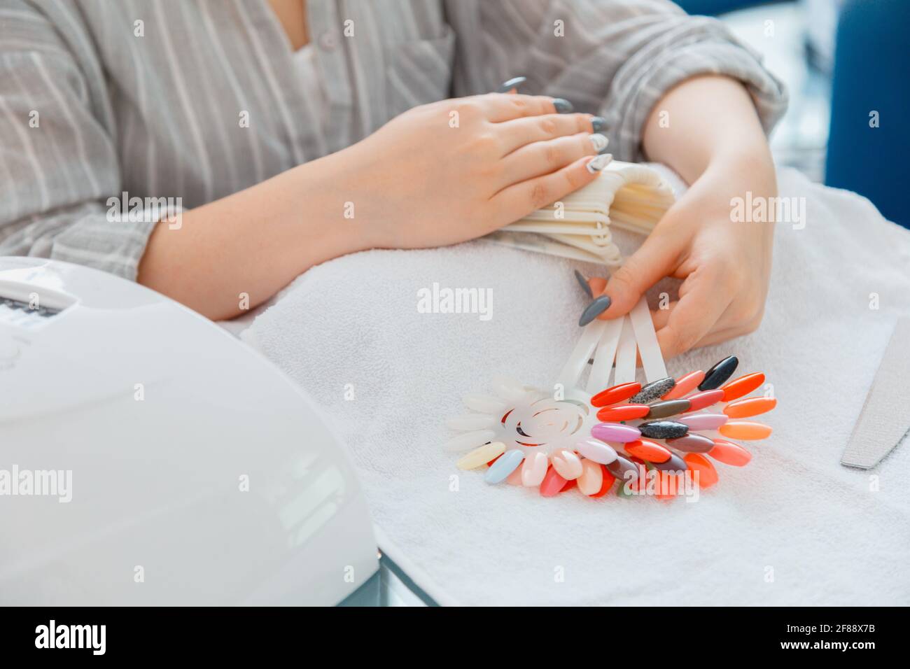 Le mani femminili con unghie acriliche artificiali raccolgo il nuovo colore di smalto per unghie durante la procedura di manicure. Processo di smalto colorato su manicure in bellezza Foto Stock