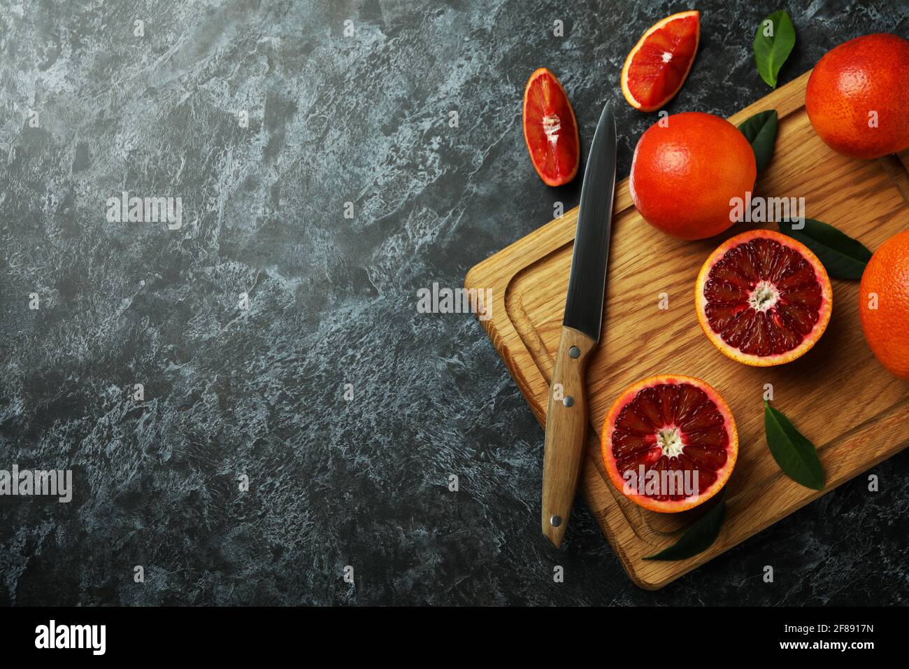 Tavola con arance rosse, foglie e coltello su tavola nera fumosa Foto Stock
