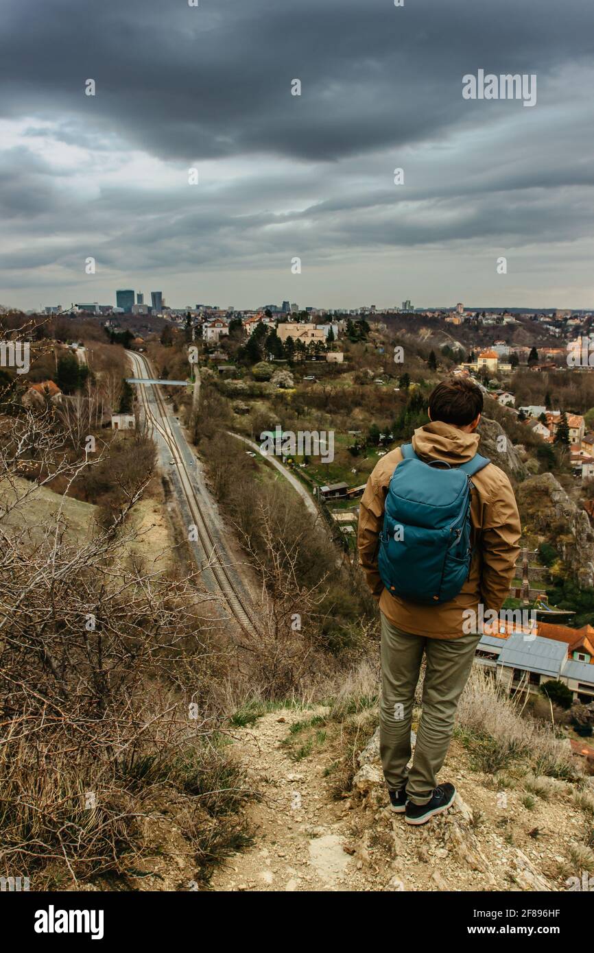 Uomo con zaino che gode di vista sulla valle di Prokopske e Praga Skyline della città, Repubblica Ceca.attraente paesaggio con profonde valli, ferrovia locale Foto Stock