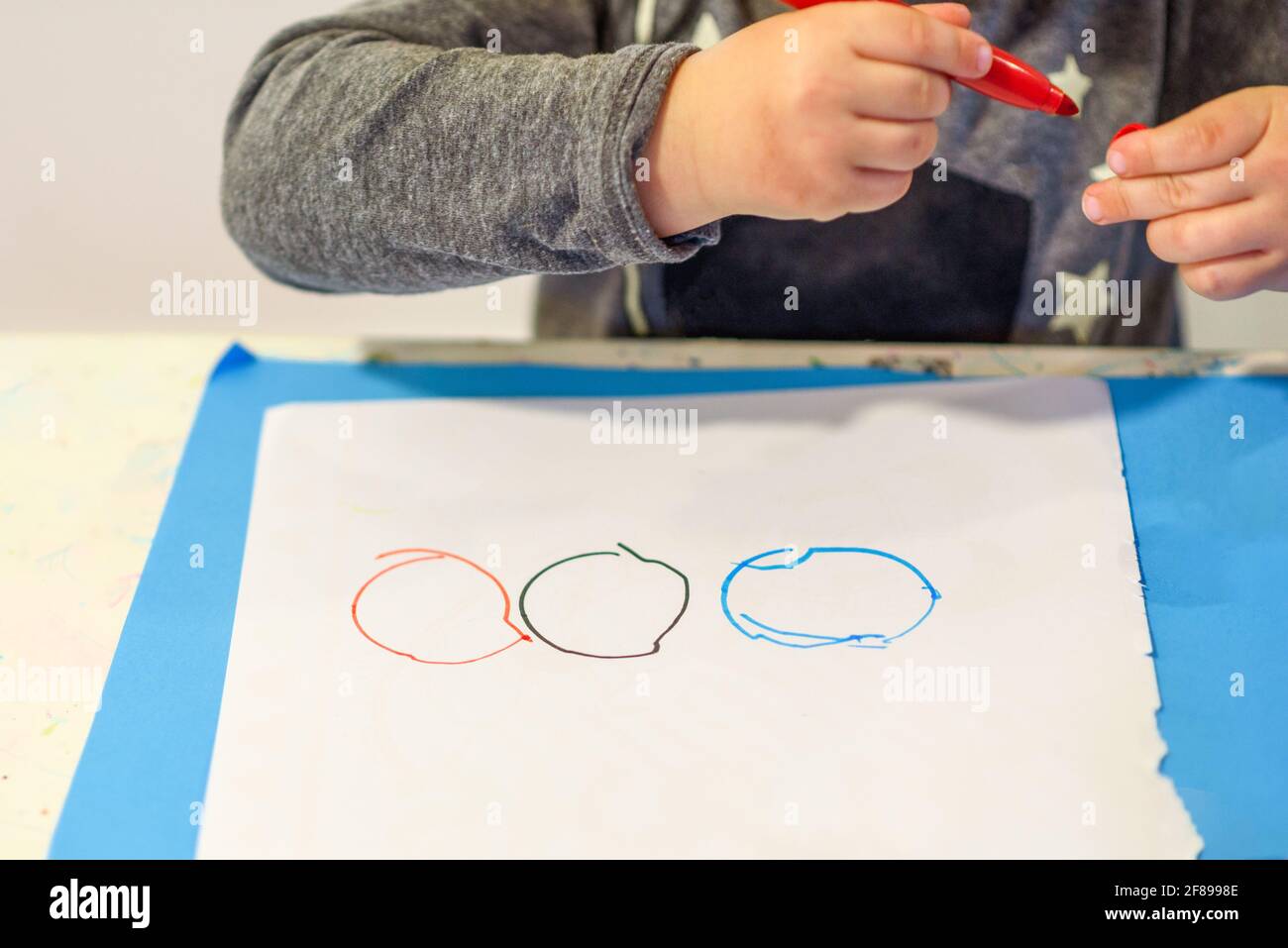 Il bambino piccolo sviluppa le abilità motorie fini, impara disegnare i cerchi. Primo piano su ragazzo carino, disegnando un anello colorato sulla carta. Foto Stock
