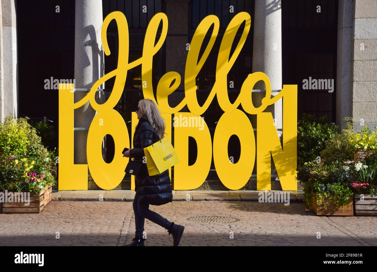 Londra, Regno Unito. 12 aprile 2021. Una donna passa accanto al cartello Hello London a Covent Garden Market. Negozi, ristoranti, bar e altre aziende hanno riaperto oggi dopo quasi quattro mesi, mentre le ulteriori regole di blocco sono rilassate in Inghilterra. Foto Stock