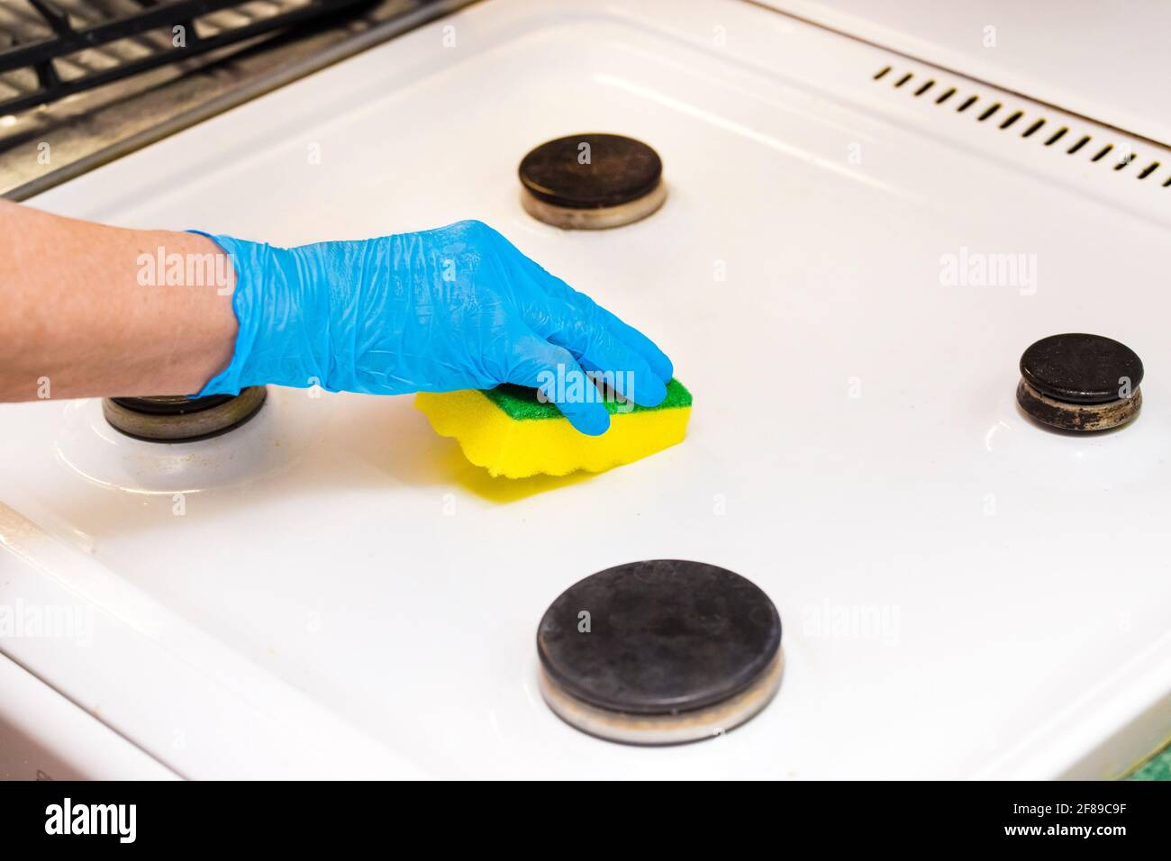 La mano della donna in un guanto domestico spugne una stufa a gas. Pulire la cucina e lavare i bruciatori. Foto Stock