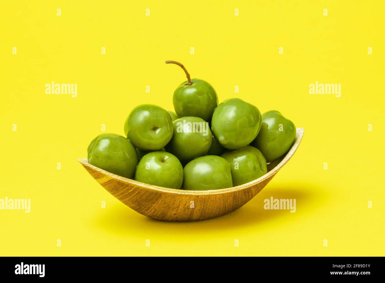 Primo piano con una ciotola di foglie di palma piena di olive verdi fresche su un tavolo giallo. Olive biologiche in un recipiente monouso. Foto Stock