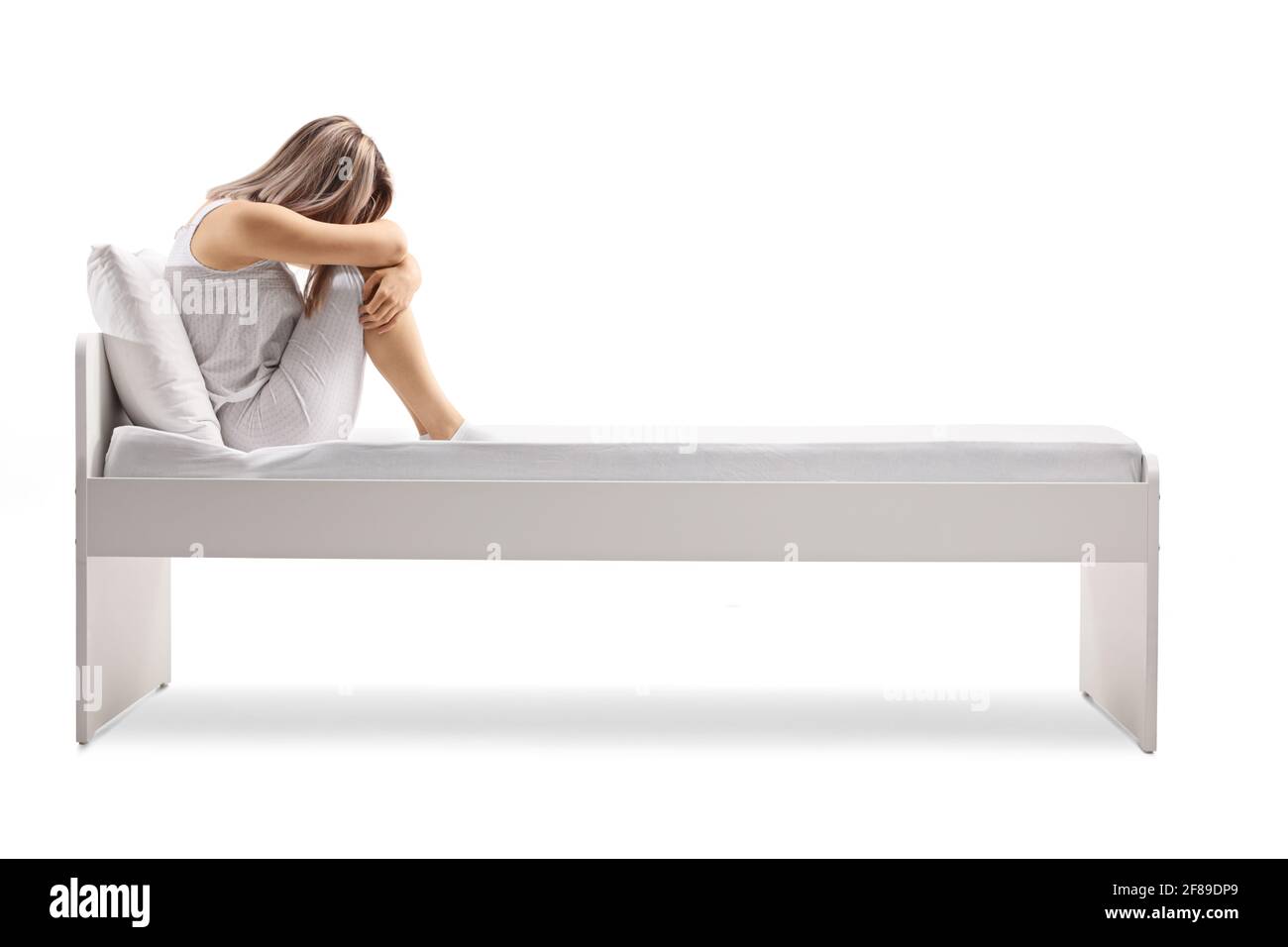 Donna triste in pigiama seduta su un letto isolato sfondo bianco Foto Stock
