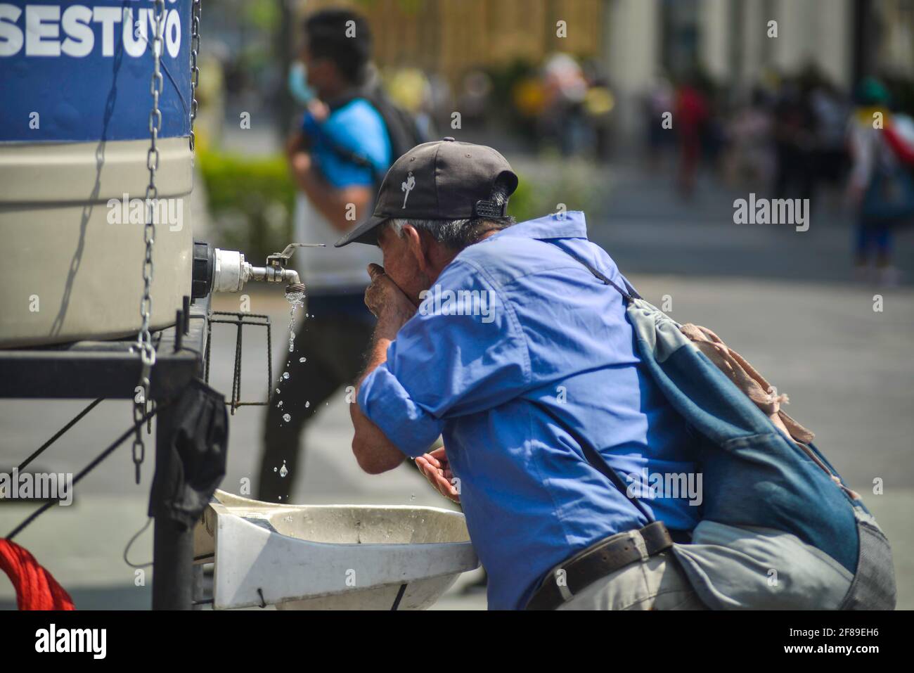 Un uomo anziano beve acqua presso la stazione di disinfezione pubblica delle mani.El Salvador riporta più di 66 mila casi confermati COVID-19 e 2,054 decessi. Foto Stock