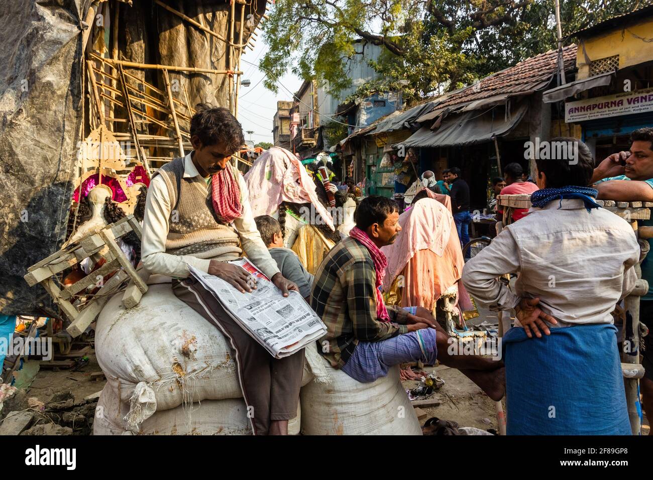 Kolkata, Bengala Occidentale, India - Gennaio 2018: Un uomo indiano che legge un giornale seduto su un mucchio di sacchi su una strada affollata a Kumartuli. Foto Stock