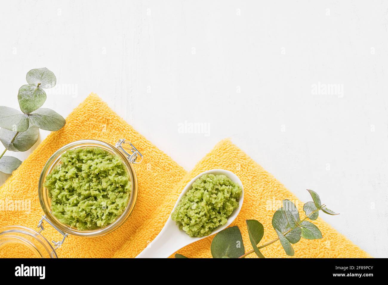 Scrub corpo verde, ramo di eucalipto, e asciugamani piegati giallo su uno sfondo di legno bianco. SPA, igiene, benessere, concetto di cura del corpo. Copia Foto Stock