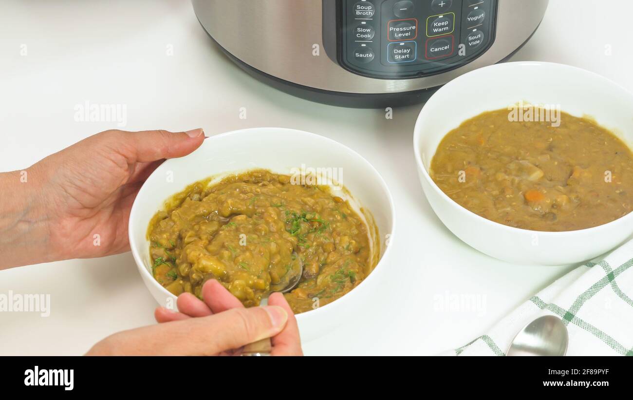 Deliziosa zuppa di lenticchie cremosa servita con aneto fresco da vicino su un tavolo da cucina bianco. Donna che mangia zuppa. Foto Stock
