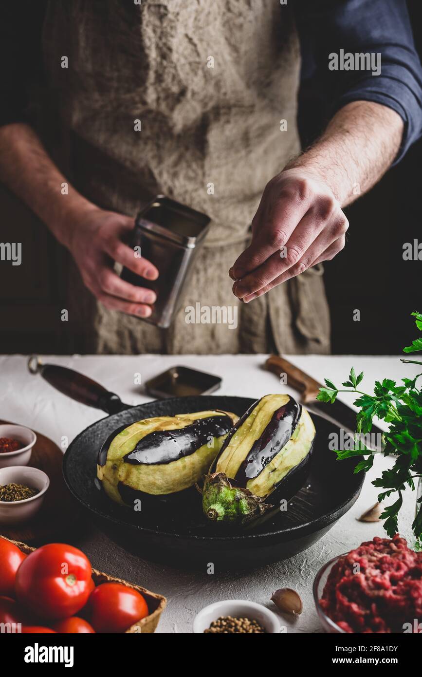 Preparazione delle melanzane per la cottura e ripieno con carne macinata e pomodori. Sale spruzzante Foto Stock