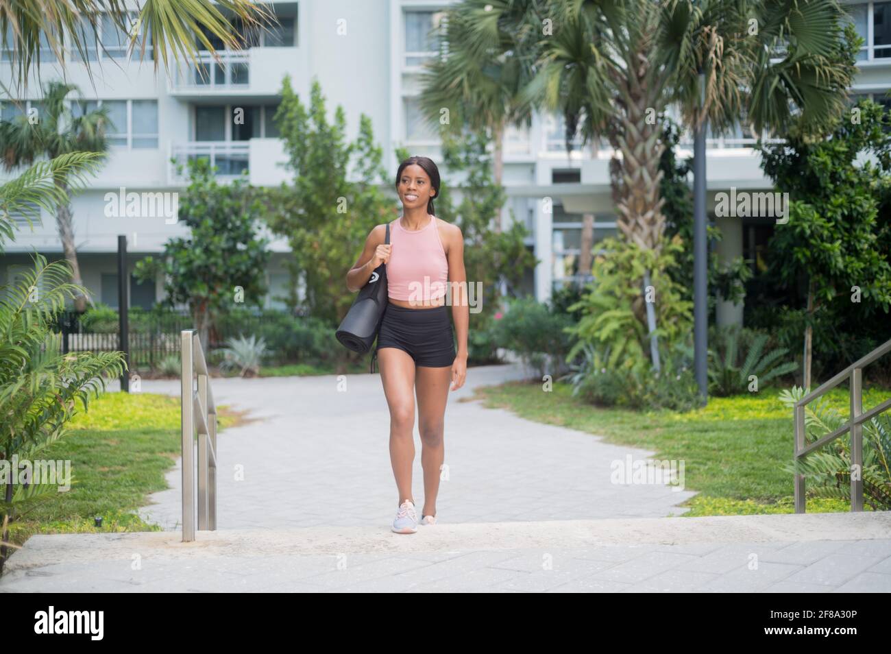 Ritratto di una giovane donna afroamericana nel camminare con tappetino yoga Foto Stock
