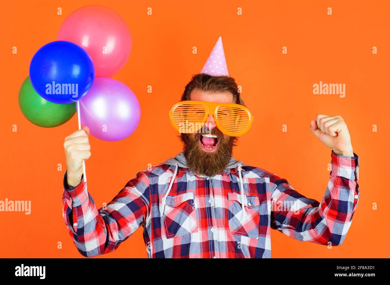 Tempo di festa. Concetto di gioia, divertimento e felicità. Uomo felice con palloncini. Uomo bearded in cappello di partito e grandi bicchieri. Foto Stock
