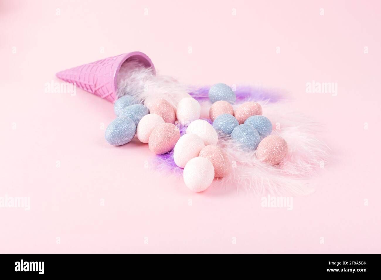 Concetto di Pasqua minimo. Cono gelato con uova color pastello su piume su sfondo rosa. Spazio di copia. Foto Stock