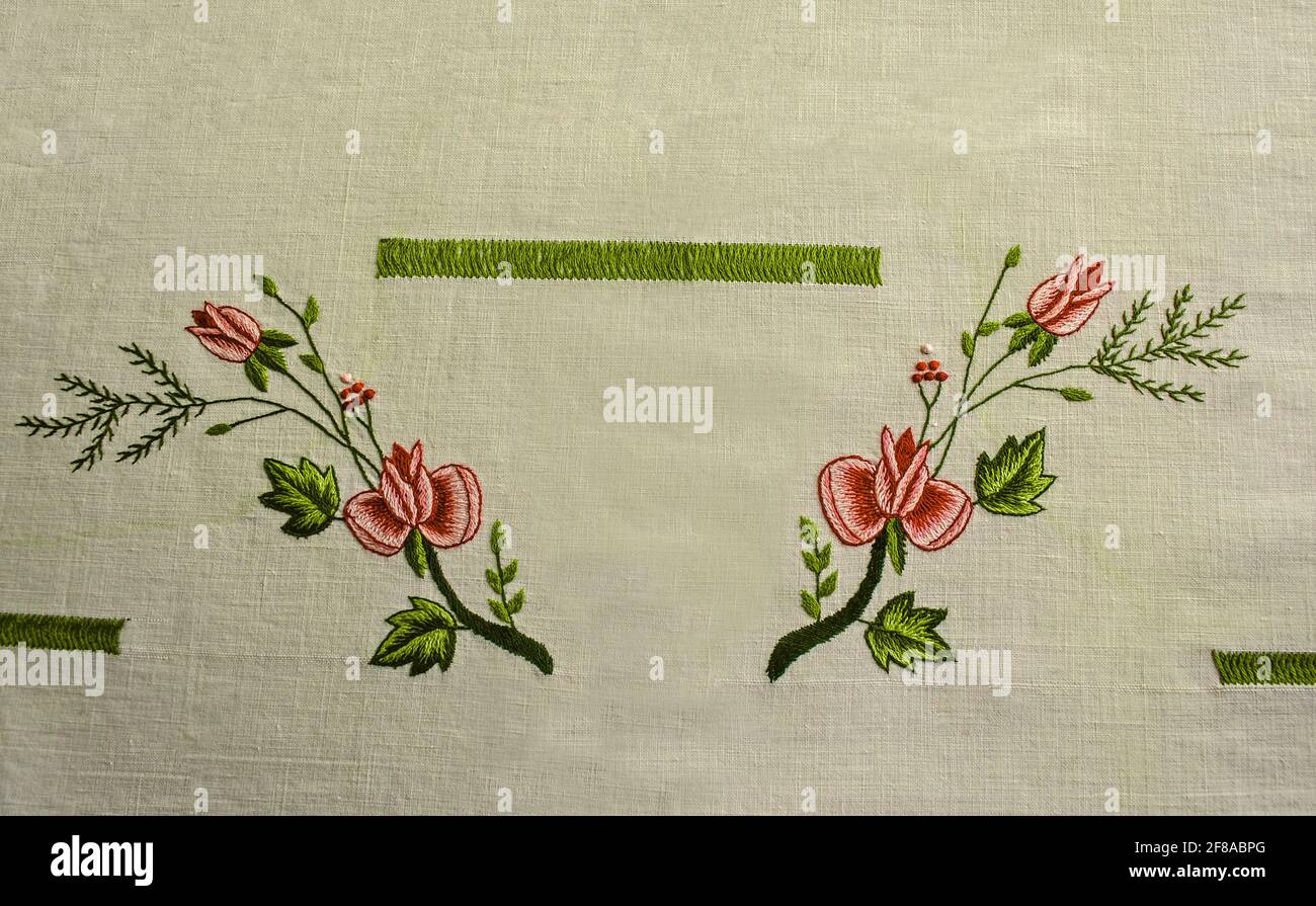 Due rami ricamati in maglia raso con rose e boccioli, rami di conifere, bacche e nastri verdi su tessuto di cotone bianco. Foto Stock