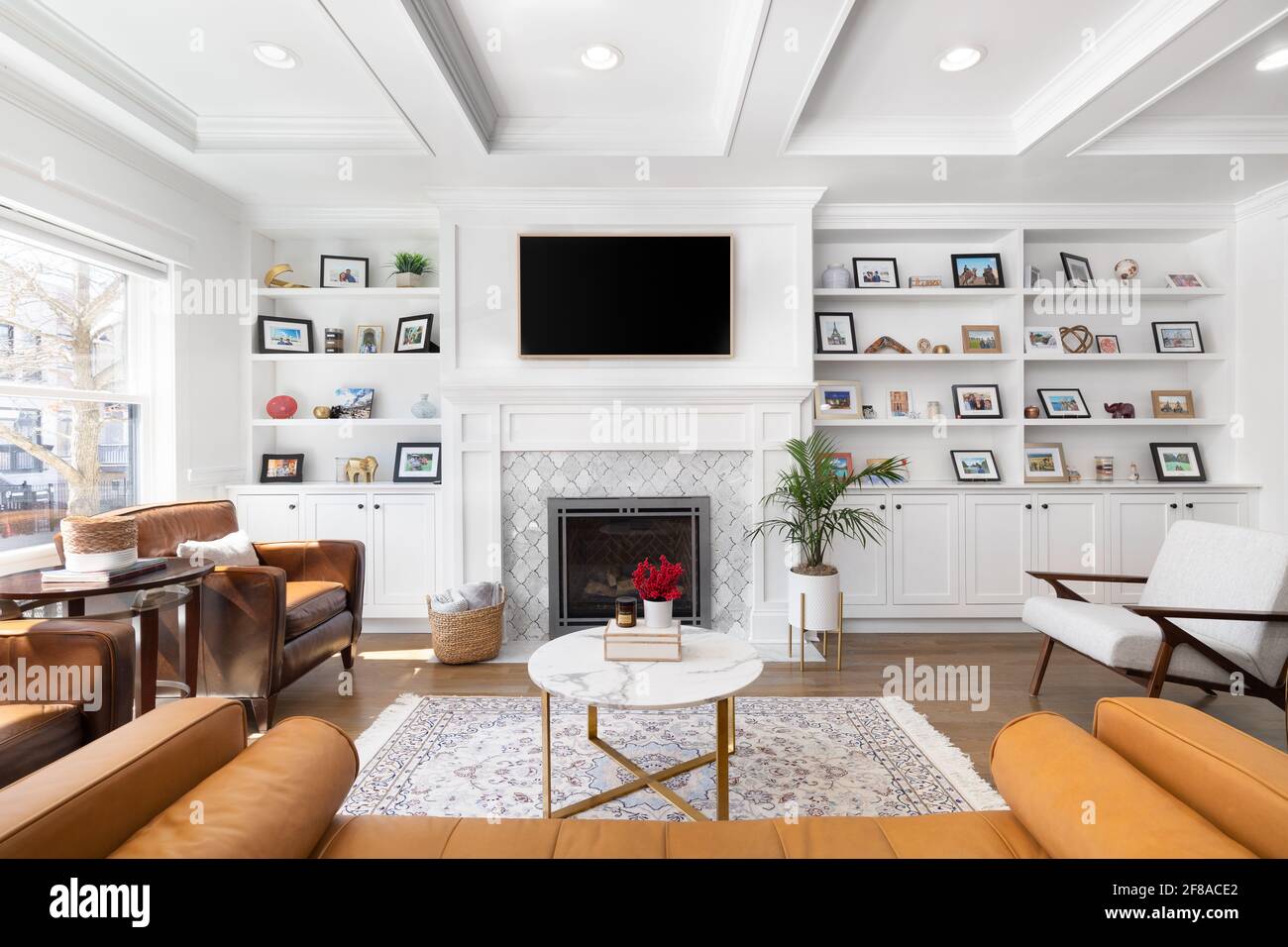Un lussuoso soggiorno bianco con soffitto a cassettoni, un televisore  montato sopra un camino piastrellato e una scaffalatura Foto stock - Alamy