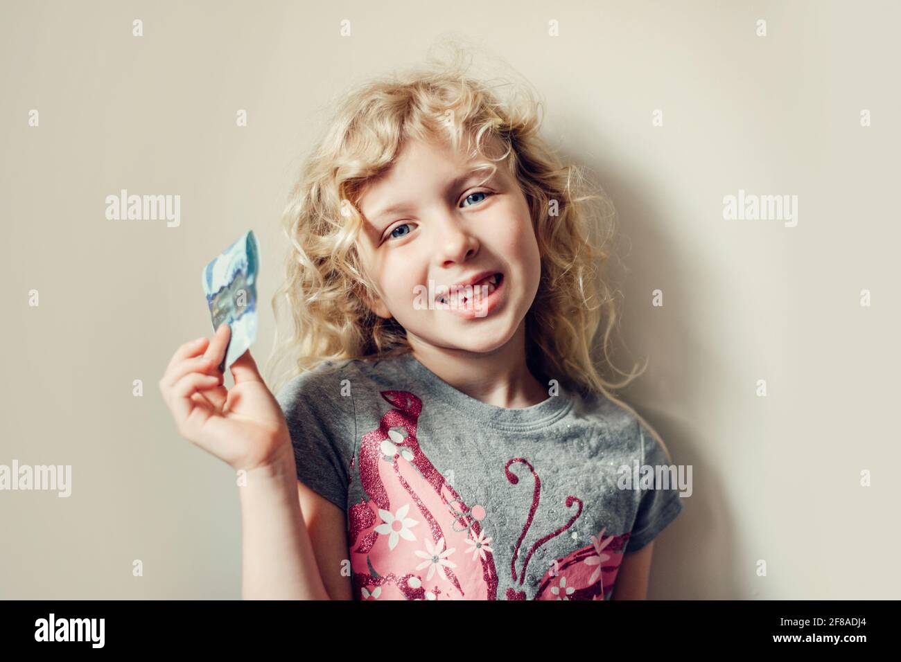 Caucasica bionda ragazza mostrando il suo dente mancante in una bocca e tenendo i soldi dalla fata del dente. Bambino orgoglioso che mostra il dente perso. Crescere in su fase uno Foto Stock