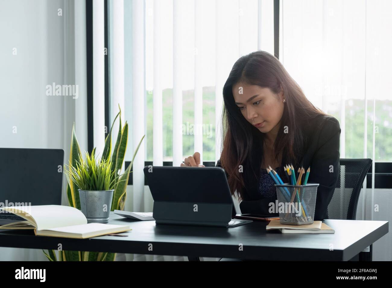 Donna d'affari che lavora con una penna stilo su un tablet digitale con un computer portatile in un ufficio moderno. Foto Stock