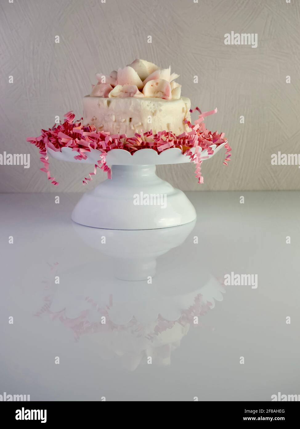 Piccola torta bianca con fiori ghiacciati bianchi e rosa sulla parte  superiore, seduta su un letto di carta rosa su un piatto di torte bianche  rialzate, delizioso dessert Foto stock - Alamy