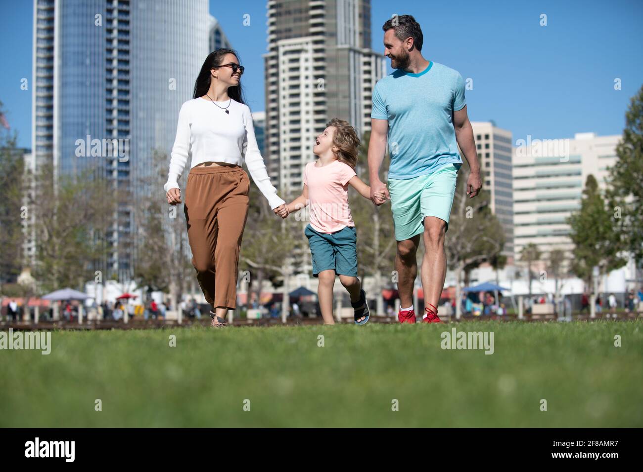 Genitori con figli che camminano in città. Famiglia facendo una passeggiata sulla strada. Madre, padre e bambini in vacanza sullo sfondo di grattacieli a San Diego. Foto Stock