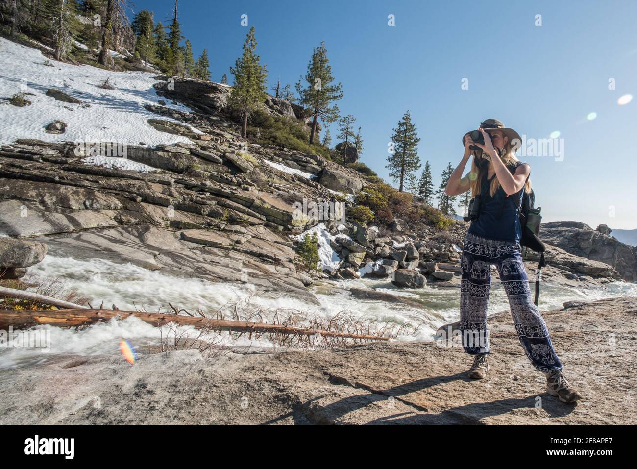 Una fotografa femminile si prende un momento per scattare una foto lungo un tratto panoramico di fiume e montagne nel parco nazionale di Yosemite, California. Foto Stock
