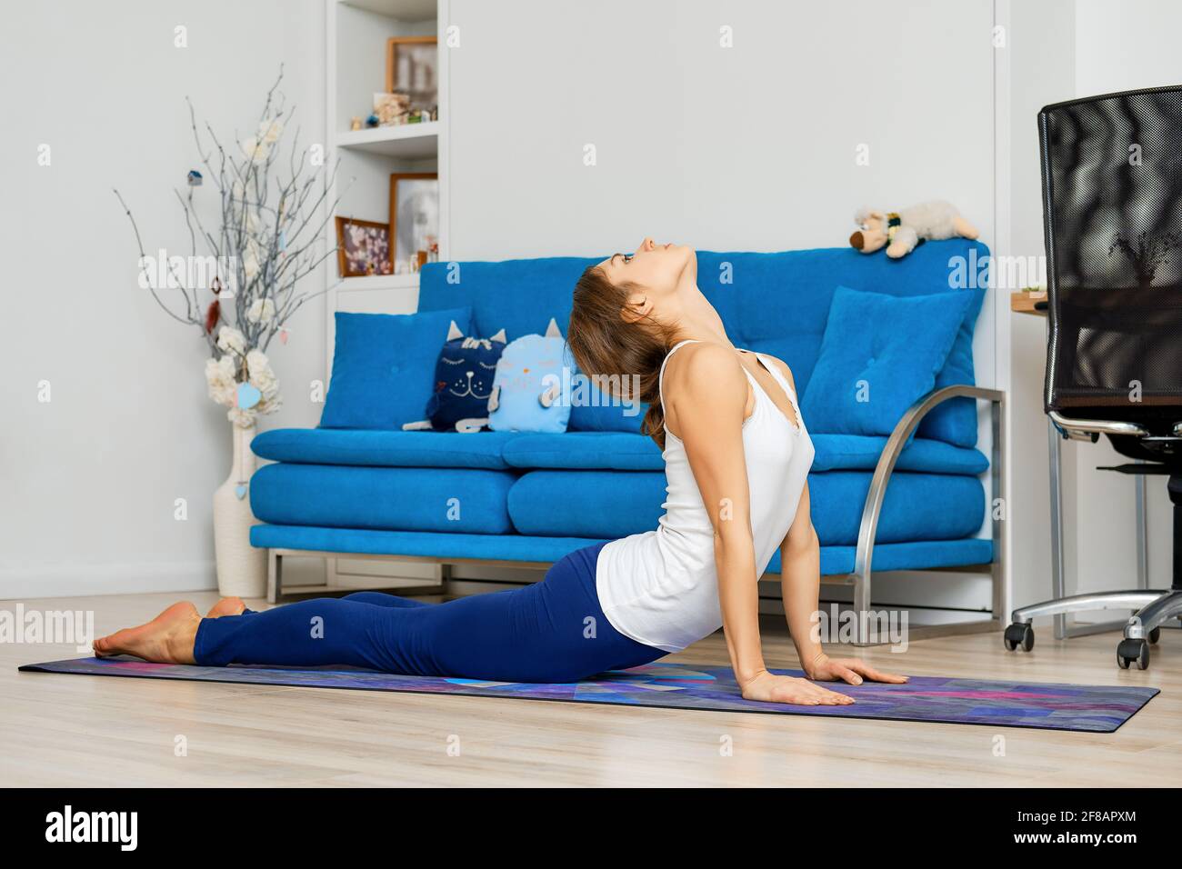 Ritratto a lunghezza intera di giovane donna che fa la posa di yoga di cobra a casa Foto Stock