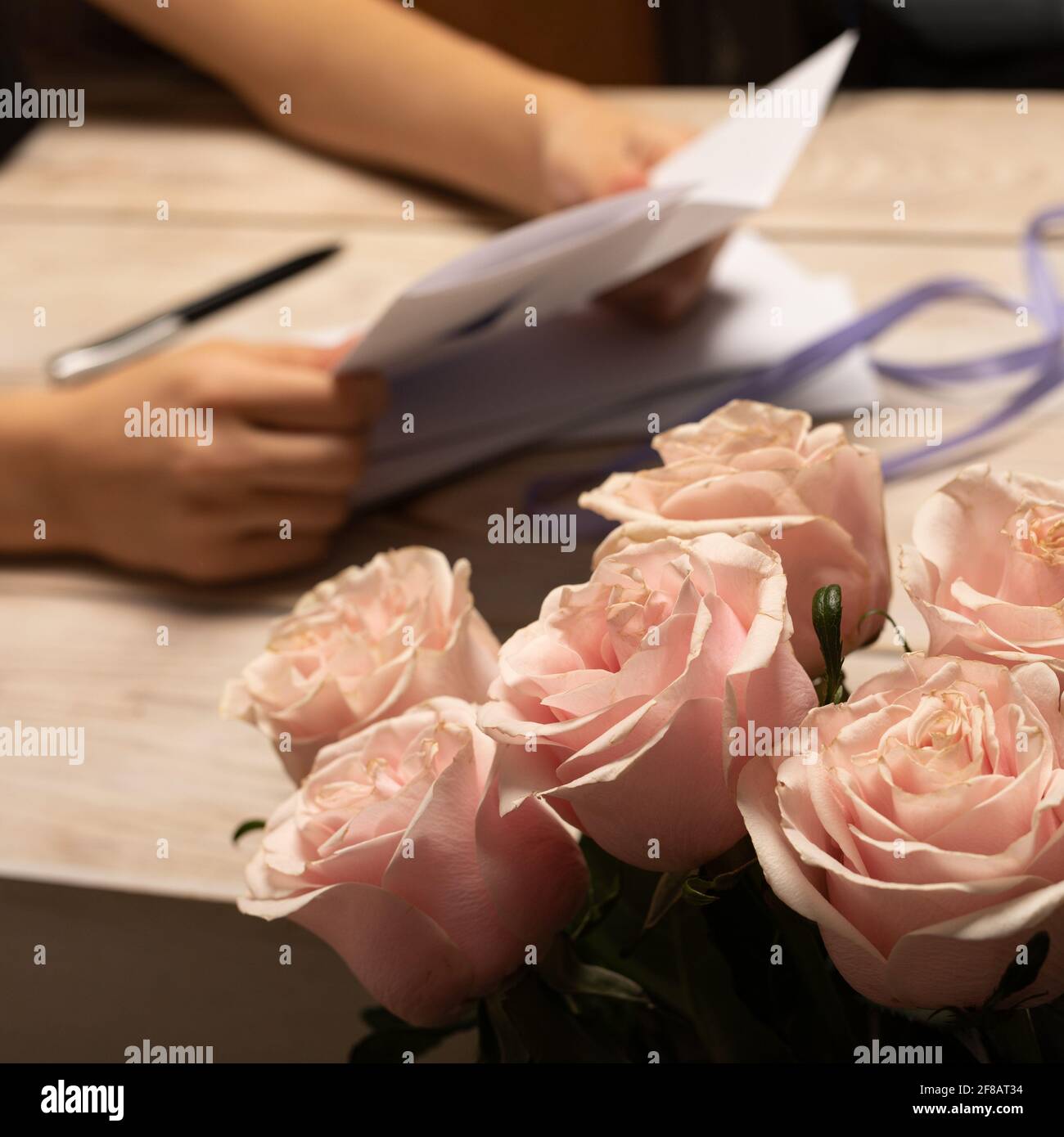 Fiori di bouquet di diverse rose rosa molle primo piano su sfondo sfocato di mani che tengono una lettera aperta o brochure sul tavolo con manico scuro. Une Foto Stock