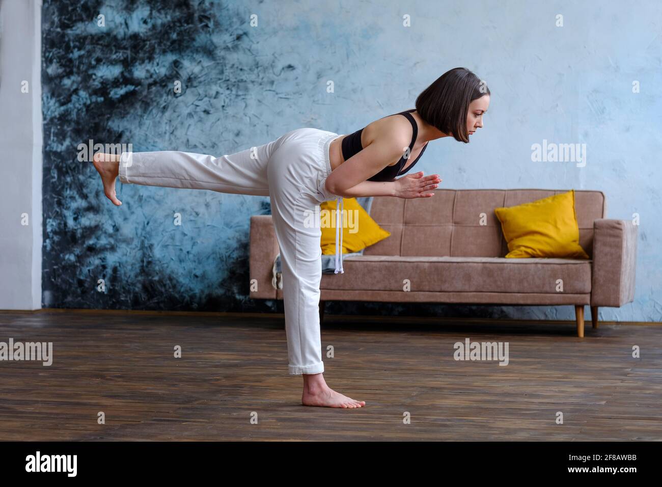 Bella donna che fa yoga alle finestre di casa, Virabhadrasana III , Guerriero posa III Foto Stock