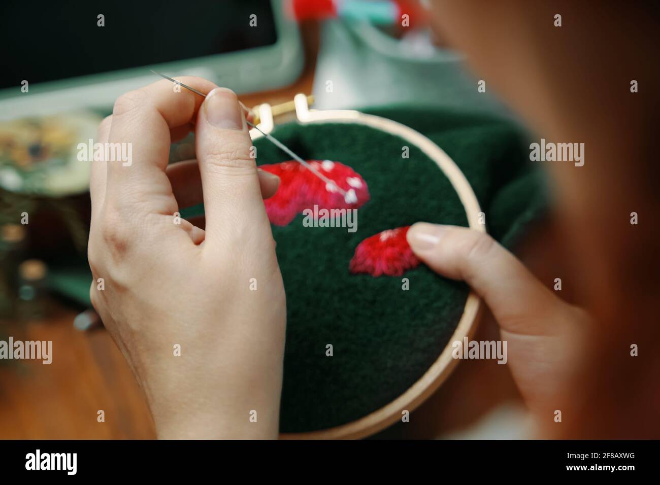 Le mani della donna cucito su un panno verde. Ricamo con filo di cotone di cappello di funghi. Concetto di lavoro a superfluo. Artigianato e fatti a mano. Foto Stock