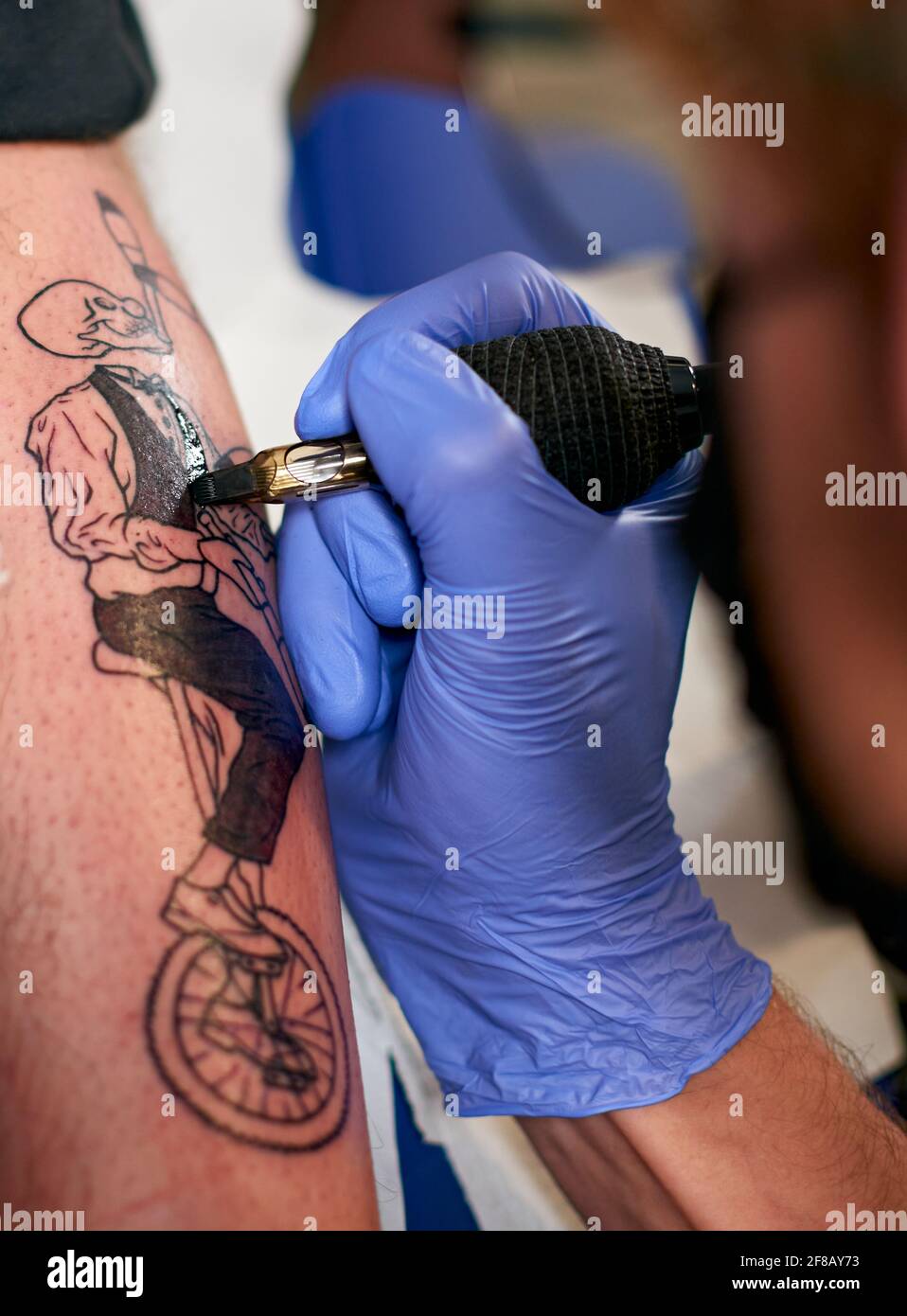 Mani in guanti blu di un artista tatuaggio che fa un tatuaggio scheletro  sulla gamba di un maschio in a. studio Foto stock - Alamy