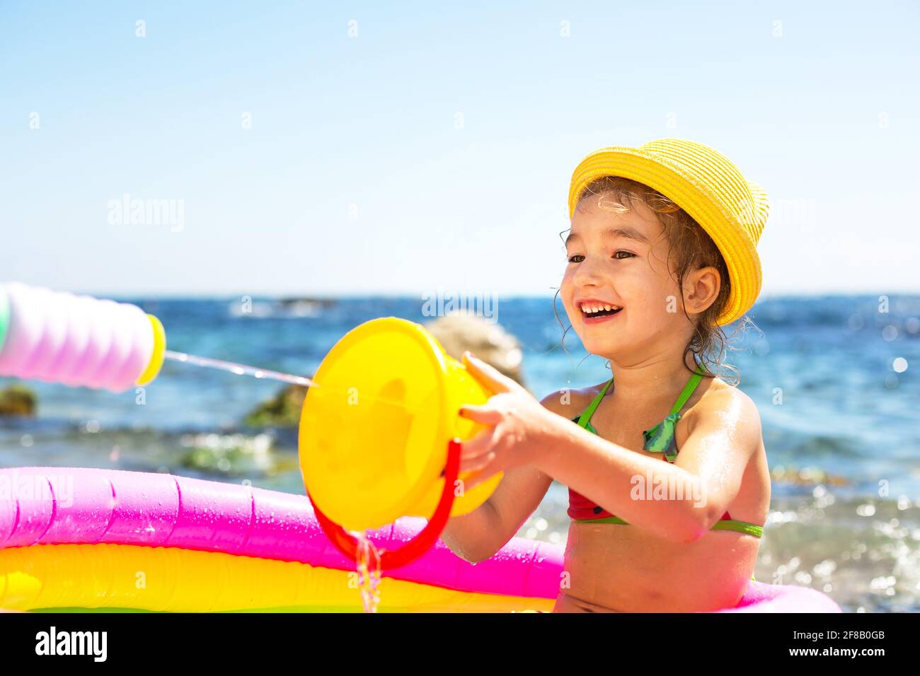 Ragazza in giallo cappello di paglia gioca con il vento, l'acqua e un  distributore d'acqua in una piscina gonfiabile sulla spiaggia. Prodotti  indelebili per proteggere i bambini Foto stock - Alamy