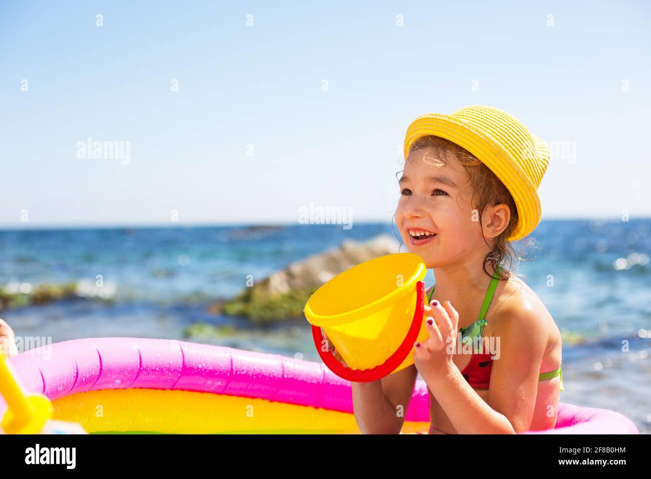 Ragazza in giallo cappello di paglia gioca con il vento, l'acqua e un  distributore d'acqua in una piscina gonfiabile sulla spiaggia. Prodotti  indelebili per proteggere i bambini Foto stock - Alamy