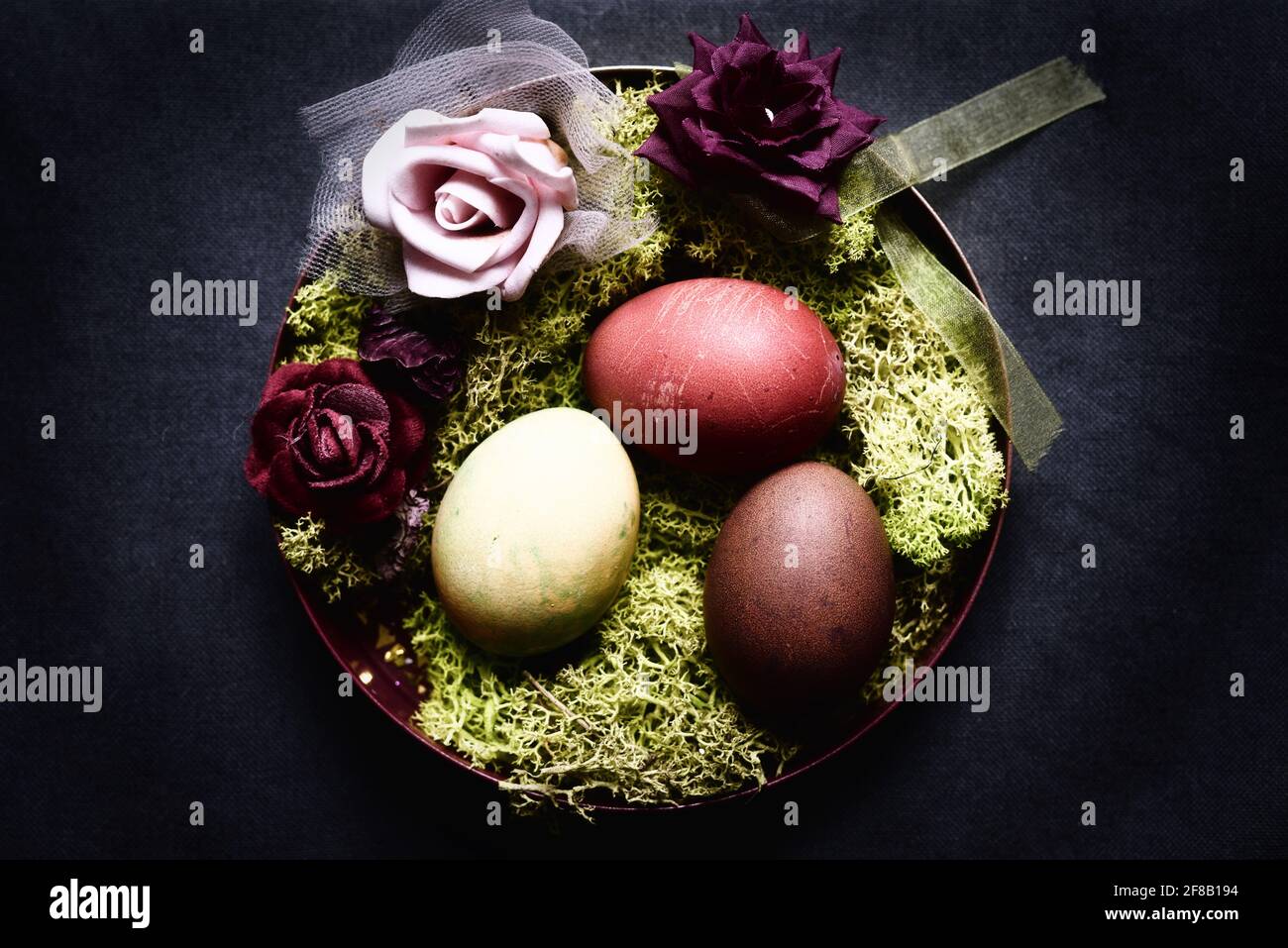 tinti le uova di pasqua in una ciotola decorativa con muschio e. rose Foto Stock