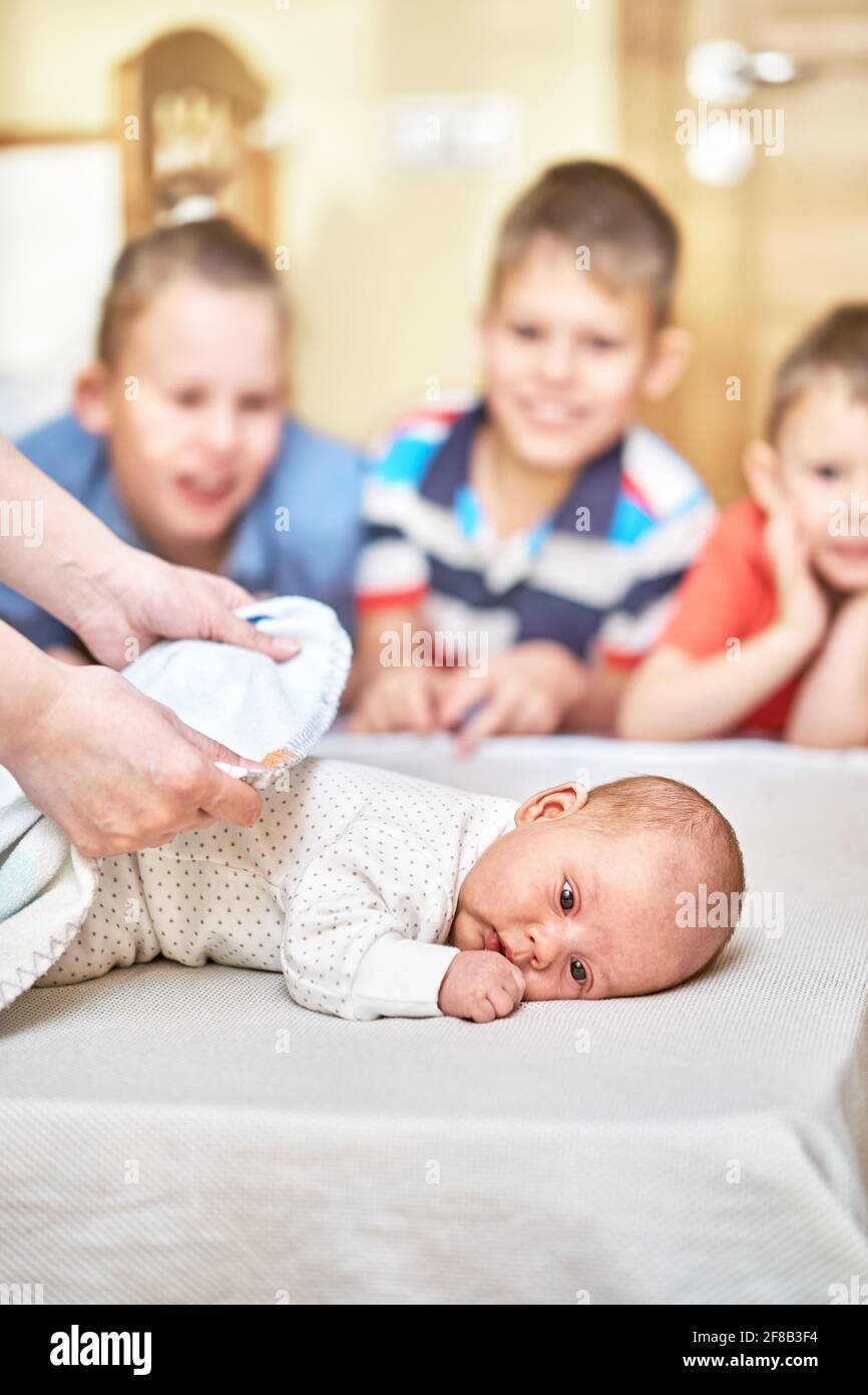 Le mani della madre delicato coprono il bambino piccolo neonato con morbido minuscolo coperta bianca contro i frati che ridono sullo sfondo Foto Stock
