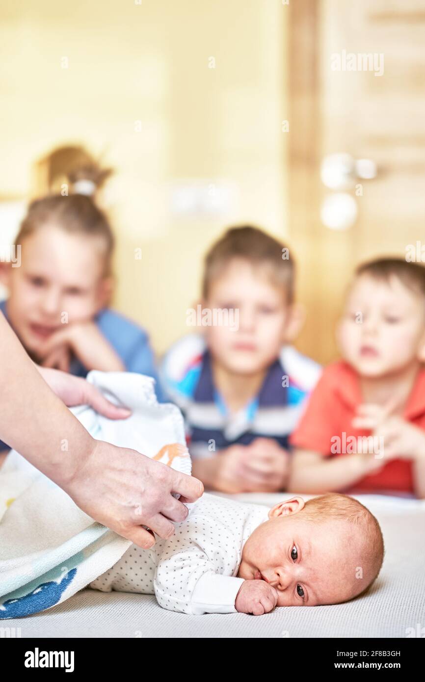 Le mani della madre delicato coprono il bambino piccolo neonato con morbido minuscolo coperta bianca contro i fratelli sfocati sullo sfondo Foto Stock