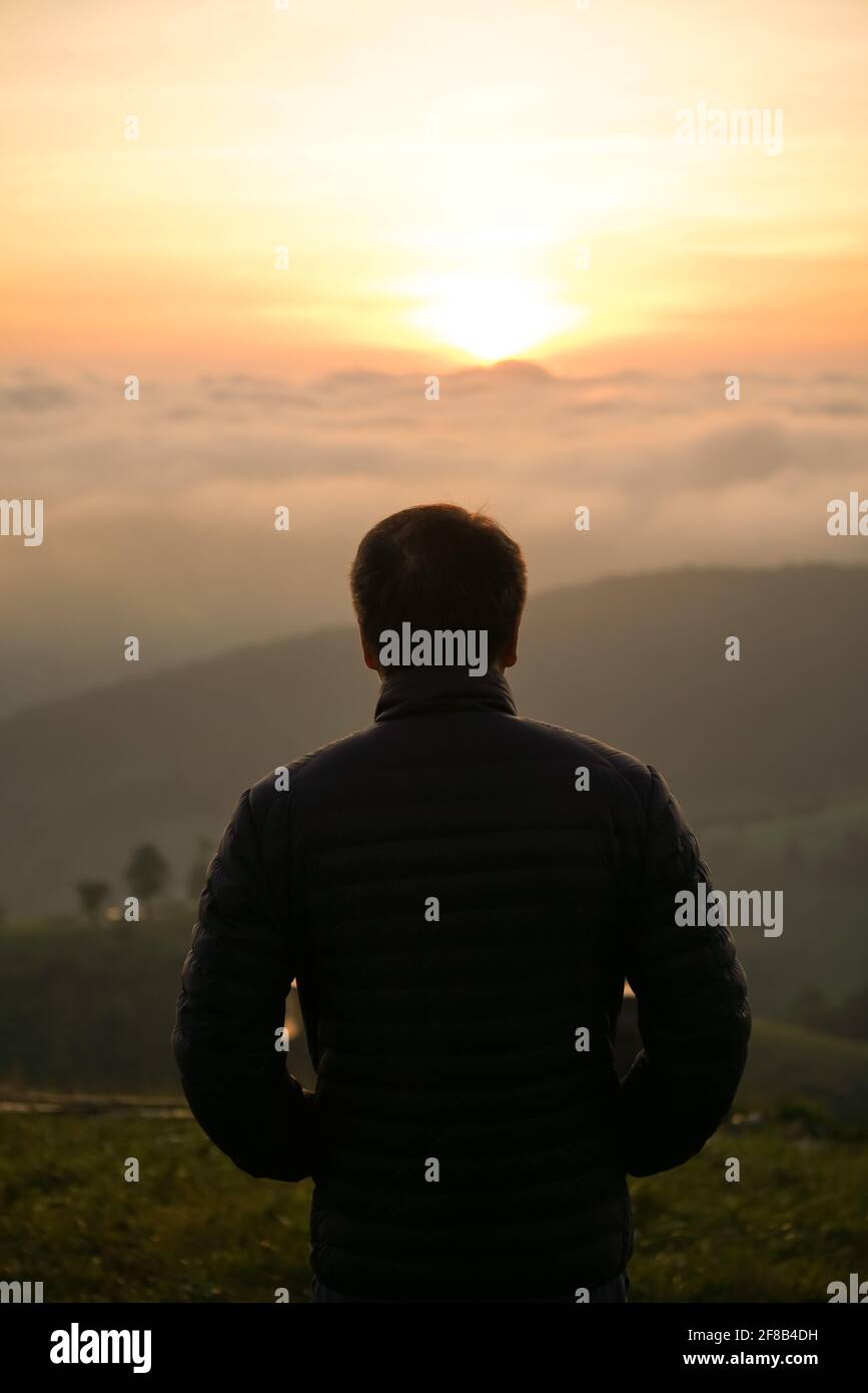 uomo che guarda l'alba da solo in cima alla collina Foto Stock